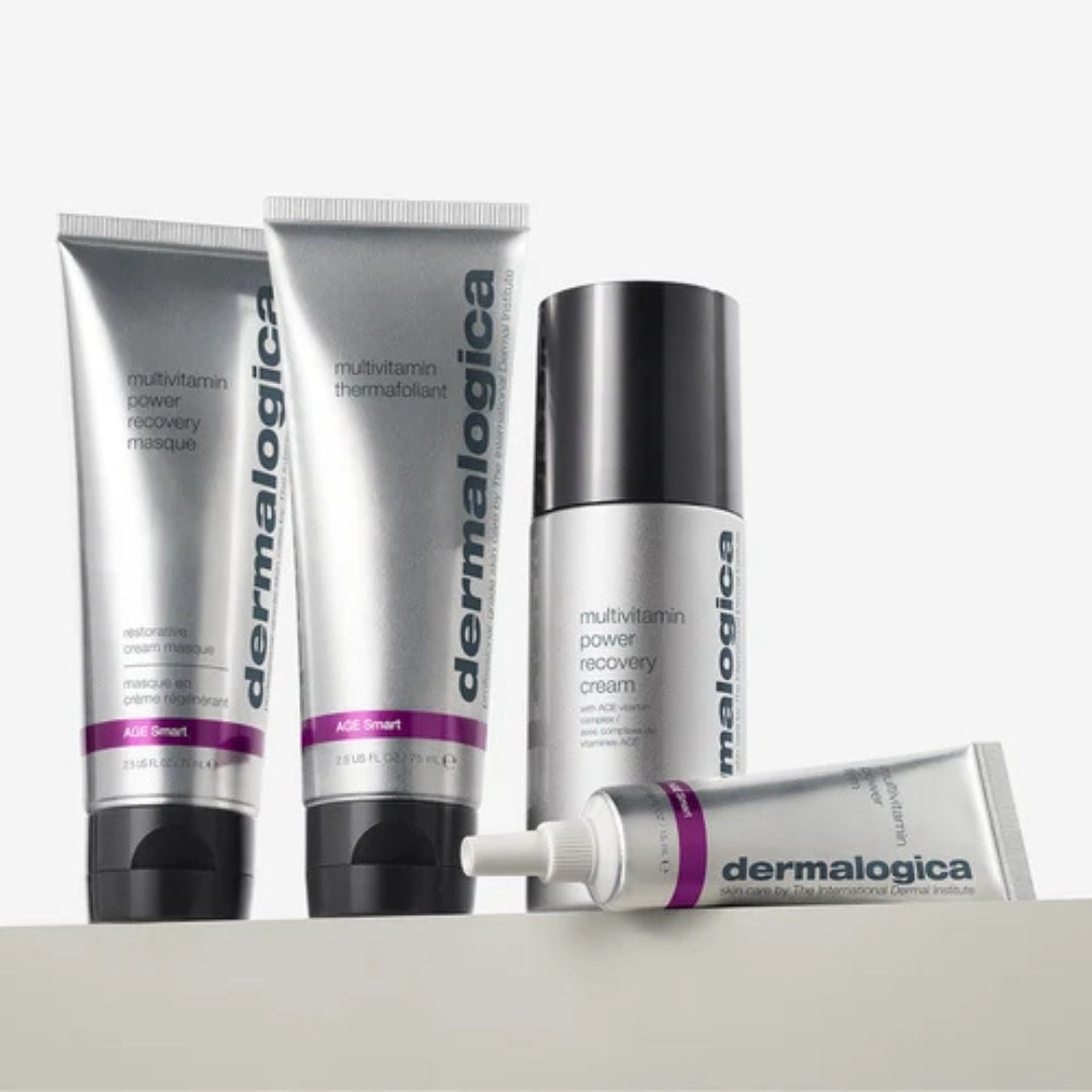 Vier Hautpflegeprodukte von Dermalogica aus der AGE Smart-Serie in silberner und violetter Verpackung sind auf einer hellen Unterlage vor einem weißen Hintergrund zu sehen.
