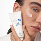 Eine Person hält eine Tube des Image Skincare - IMAGE MD barrier repair recovery balm in der Nähe ihres Gesichts und streicht den Balsam auf ihre Wange, um die Anwendung der Hautpflege zu demonstrieren.