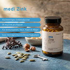 Eine Flasche medigevity medi Zink steht auf einer hölzernen Oberfläche mit verstreuten Kapseln, einem Schlüssel, Kürbiskernen und Beeren. Das Etikett hebt Zinkbisglycinat, 25 mg pro Kapsel, zur Unterstützung von Immunsystem, Haut, Haaren und Nägeln hervor.