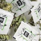 Mehrere Tütchen LPG - 14 Tage Express Bio Abnehmtee sind auf belaubten Zweigen ausgestellt. Die weißen Tütchen mit botanischen Illustrationen und grünen Akzenten tragen auf der Vorderseite den Markennamen LPG und Angaben zum Produkt.